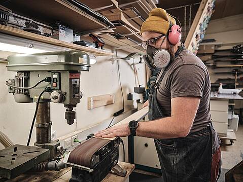Bild von Lexware: Handwerker mit Mundschutz bei der Arbeit an einer Schleifmaschine